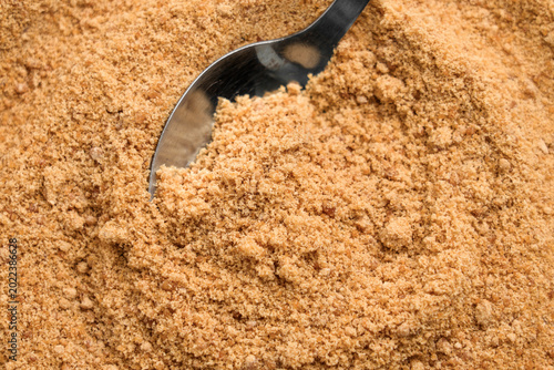 Spoon filled with raw brown sugar in heap of granulated crystals