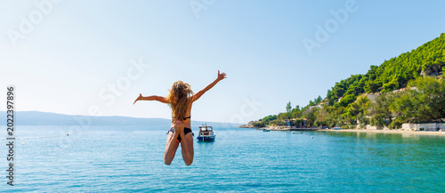 Obraz na płótnie Happy young woman in bikini jumping into turquoise sea water with arms raised du