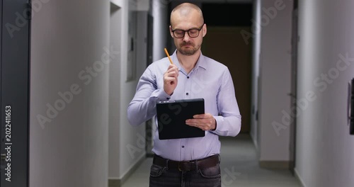 Businessman stands in corridor and writes detailed notes in official document. Serious man with clipboard conducts thorough inspection of modern residential building