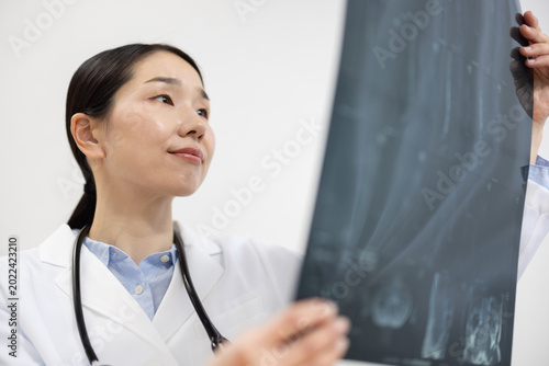 Schilderij op canvas Asian Female Doctor in White Coat Reviewing X-ray Image