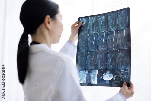Schilderij op canvas Asian Female Doctor in White Coat Reviewing X-ray Image