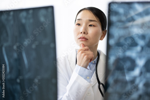 Schilderij op canvas Asian Female Doctor in White Coat Reviewing X-ray Image