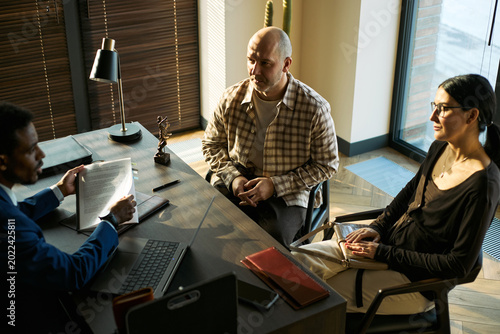 Fotografie Medium shot of middle aged couple meeting lawyer, reviewing documents during divorce consultation and legal separation process