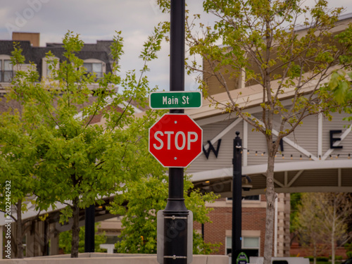 Obraz na plátně Red stop sign and green Main St street sign on a black pole in a downtown urban