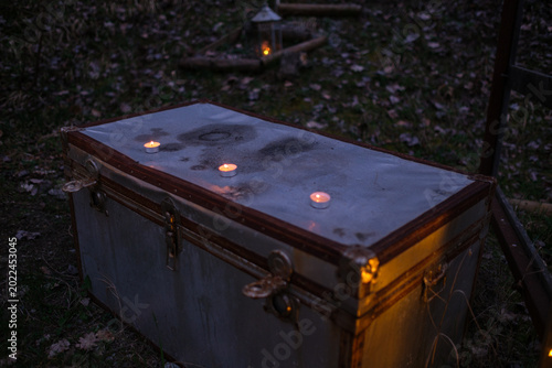 Moonlit Metal Trunk Topped With Candles, Resting On Leafstrewn Grass Outside Castello Bianello, Amber Flames