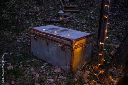 Moonlit Metal Trunk Topped With Candles, Resting On Leafstrewn Grass Outside Castello Bianello, Amber Flames