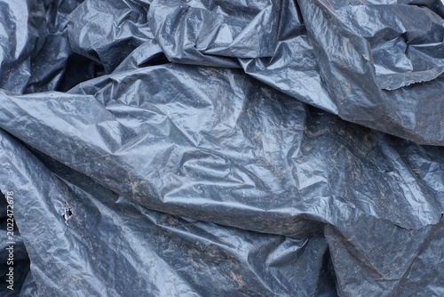 Plastic texture of a piece of dirty crumpled black cellophane in the street