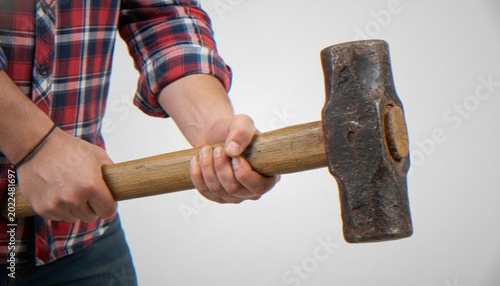 Tableau sur toile A close-up shot of a person in a plaid shirt holding a heavy sledgehammer against a white background