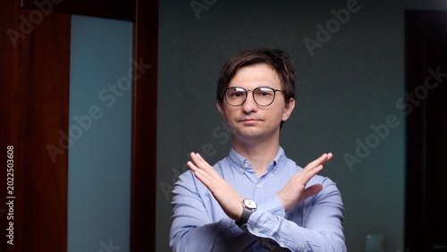 Fényképezés Young man in round glasses and blue shirt forms an x with crossed arms, conveyin