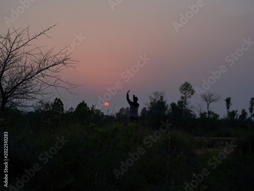 silhouette of a man taking a photo of the sun from a mobile in a forest