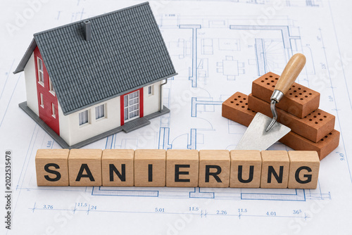 Miniature house with bricks and trowel on architectural blueprints