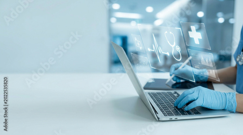 Healthcare worker in protective gear using laptop in bright medical facility
