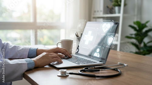 Person using laptop with stethoscope on wooden desk near window