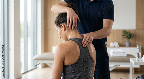 Faceless physiotherapist stretching neck of female patient in bright clinic