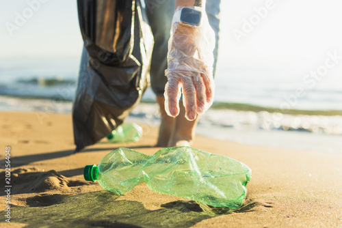 Photos Volunteer cleaning beach, wearing plastic glove and holding trash bag, picking u