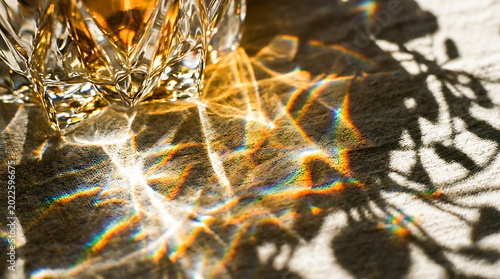 Crystal glass on beige fabric with colorful shadows and sunlight reflections transparent background