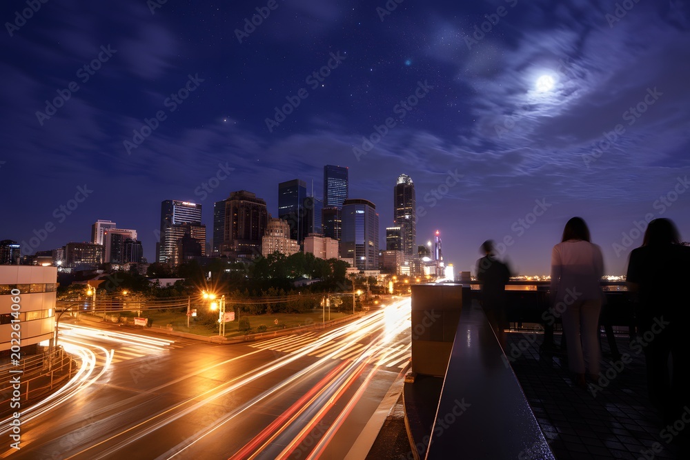 Fototapeta premium Nighttime cityscape with people overlooking road and skyscrapers