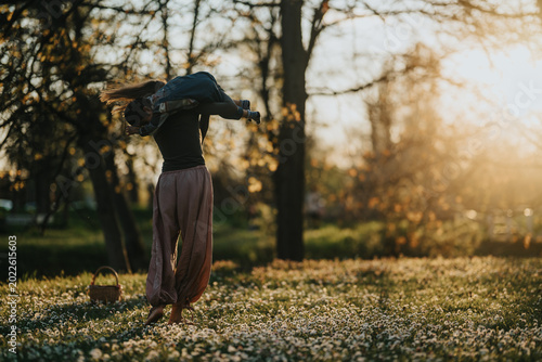 Fotografía Mother carries her child playfully over her shoulders while walking through a field of small white flowers