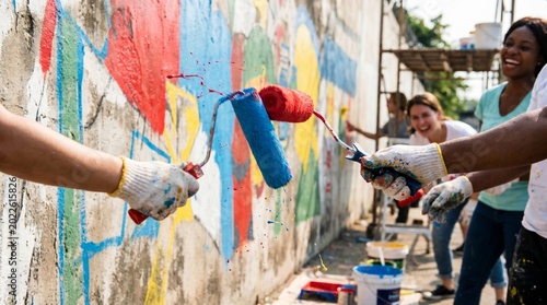 Volunteers engaging in community volunteering work with paint rollers and brushes on a colorful mural wall.