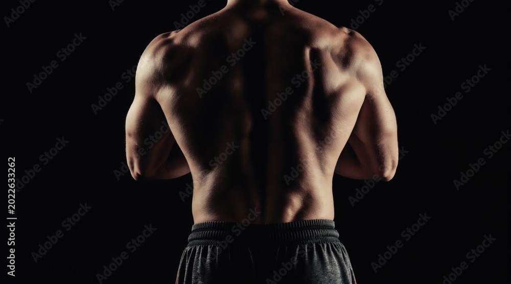 Fototapeta premium Man displays muscular back and arms, strong athletic physique, dark background, dramatic lighting accentuates muscle definition, fitness, strength training, gym workout, healthy lifestyle.