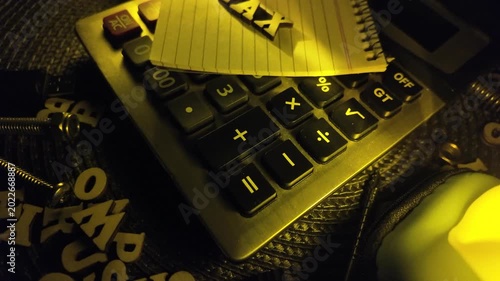 The word 'TAX' is spelled out on a yellow notepad placed on a calculator.