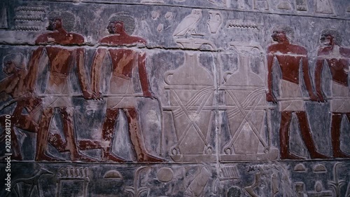 Close-up of detailed limestone relief carving inside tomb of Kagemni at Saqqara, Egypt, depicting ancient Egyptian male figures with tools, faint traces of original red pigment.