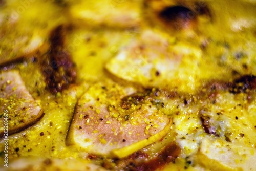Zbliżenie makro na upieczoną pizzę z topionym serem, szynką i przyprawami. Apetyczna fotografia kulinarna o płytkiej głębi ostrości, idealna do menu lub bloga.