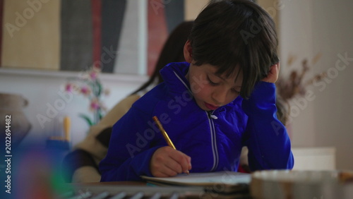 Photos Young boy concentrating on homework with pencil and notebook at table, quiet hom