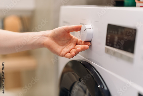 Woman adjusting washing machine program control dial in modern laundry