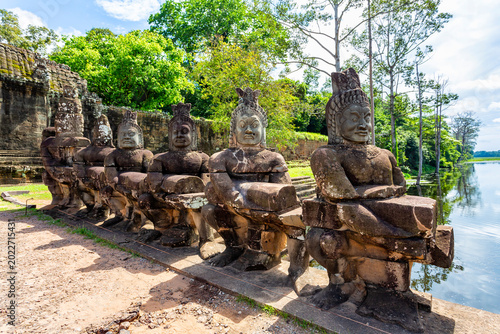 Photos A line of ancient, weathered stone statues of gods or demons stands along a caus