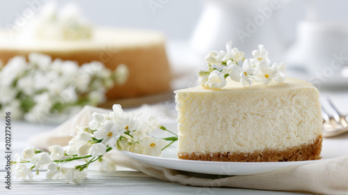 Cheesecake slice with white lilac flowers on plate and whole cake in background for Shavuot celebration