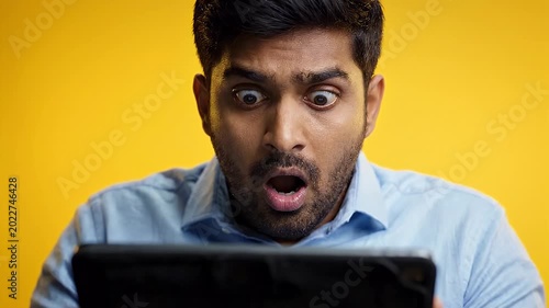 Surprised man reacting to news on tablet against yellow background