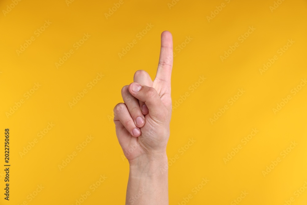 Naklejka premium Man pointing upwards on yellow background, closeup
