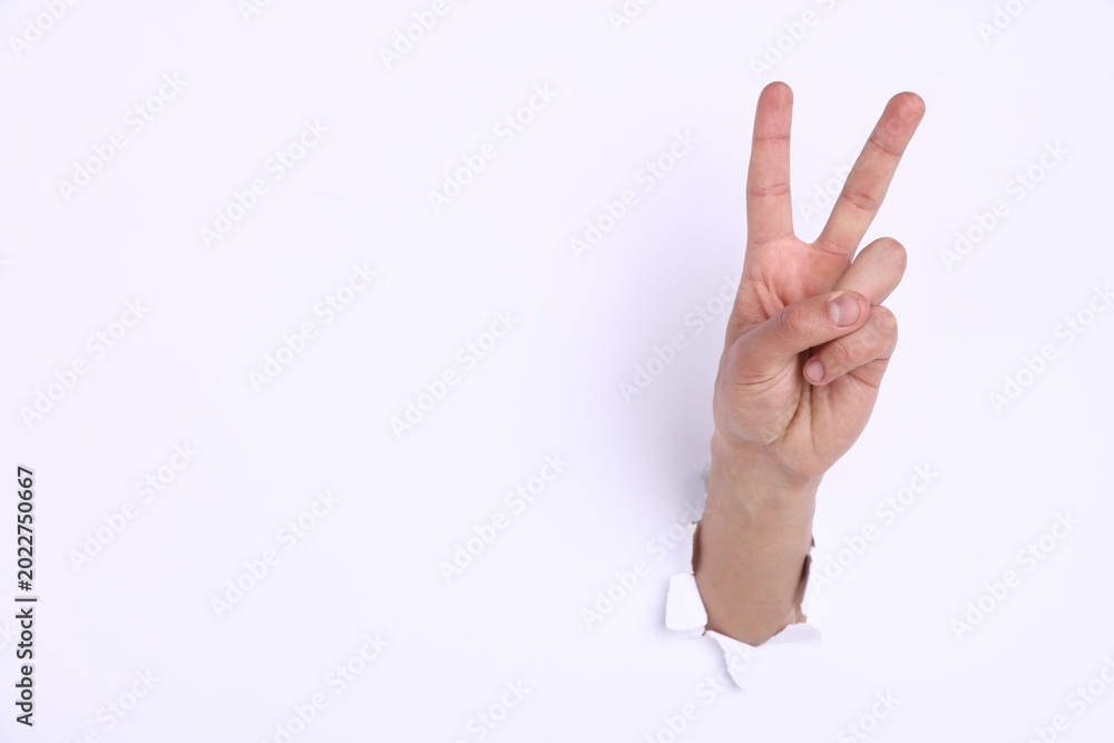 Naklejka premium Man showing number two with fingers through hole in white paper, closeup. Space for text