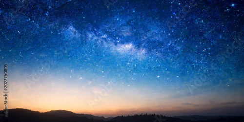 Milky Way galaxy over silhouettes of mountains at sunset, blue starry night sky background with orange horizon, breathtaking astronomical landscape photography.