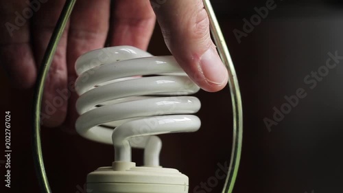 Closeup of a compact fluorescent light bulb mounted in a lamp frame against a dark wooden background.