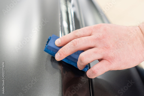 Photos The process of applying a nano-ceramic coating for hydrophobic effect on the grey matte car's hood by worker with a sponge, bottle of chemical composition, microfiber