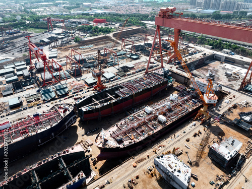 Fotografi Large shipyard scene with multiple vessel hulls under construction and heavy cra