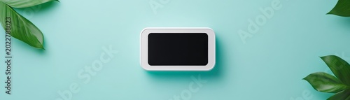 Minimalist flat lay of a white smart display with blank screen, framed by natural green leaves on a serene aqua background. A modern eco-tech device mockup. Smart home, Product display