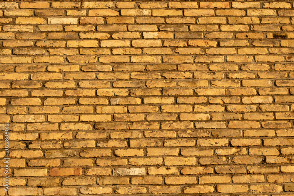 Fototapeta premium Textured background of an old yellow brick wall in warm evening sunlight. Full frame pattern of weathered sand-lime bricks with rough mortar joints.
