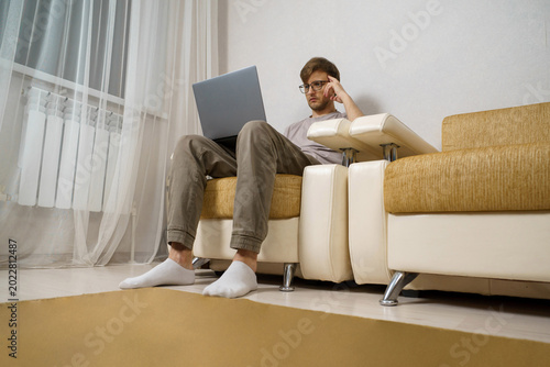 Bild auf Leinwand An adult man works from home, sitting on the couch