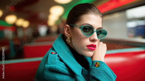 Stylish in Shades: A portrait of a woman of elegance and poise in an indoor diner setting, wearing fashionable sunglasses, a chic coat and glamorous red lipstick.  