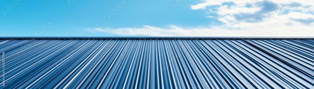Obraz premium Striking blue corrugated metal roof in a low-angle perspective against a vibrant blue sky with wispy clouds, depicting modern industrial architecture., Construction, Minimalist