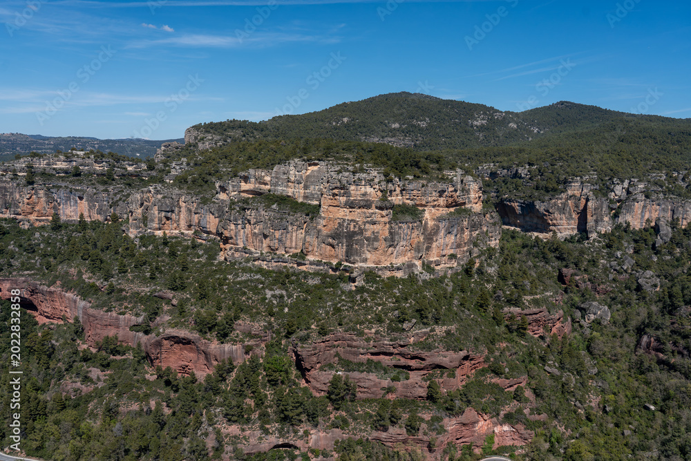 Obraz premium High-resolution landscape shot of dramatic geological formations, featuring sheer rock walls and pine-covered ridges under a clear blue sky.