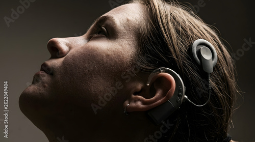 Close-up profile of an adult woman in her 30s wearing a cochlear implant and hearing aid device on her ear, looking upwards. Generative AI.