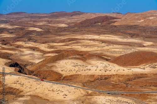 Εκτύπωση καμβά A red car on a lonely road contrasts sharply with the inhospitable, arid, and volcanic landscape