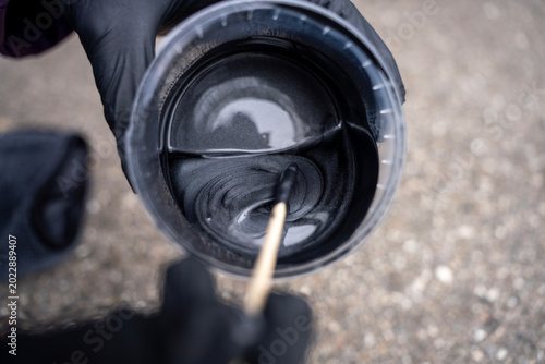 Canvastavla Hands in black nitrile gloves stirring silver metallic automotive paint in a plastic jar with a wooden stick, preparing car paint for refinishing or body repair service