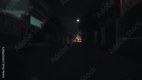 Low angle dark empty street at night illuminated by dim streetlights creating a moody atmospheric and spooky scene