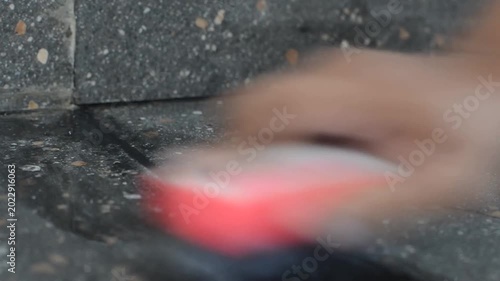 Low angle of a hand scrubbing a dark stone tile wall or floor with a red sponge