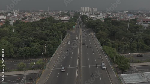 Shot in D-Log M Aerial view of a highway bridge overpass with vehicle traffic leading toward a distant city skyline under overcast skies